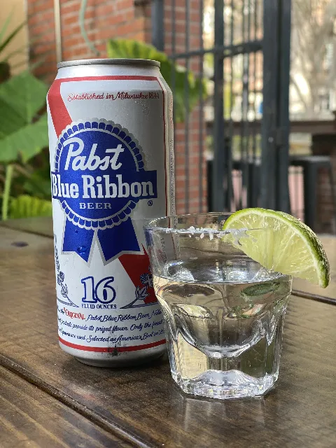 a can of pbr and a shot of tequila with a lime and salt on an outside table