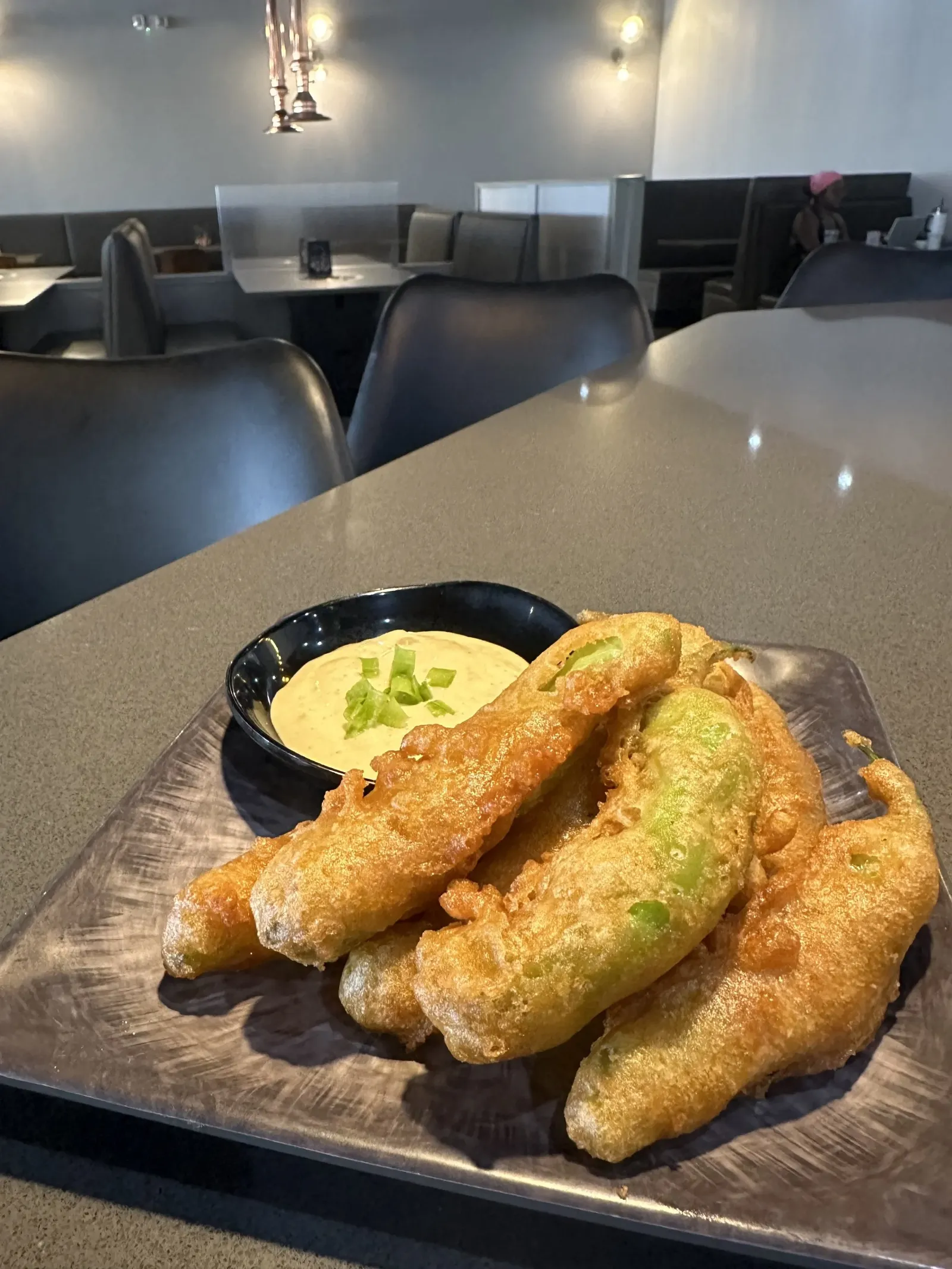 Plate of fried stuffed peppers with dipping sauce on a restaurant table.