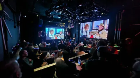 People watching a sports event on multiple screens in a dimly lit room.