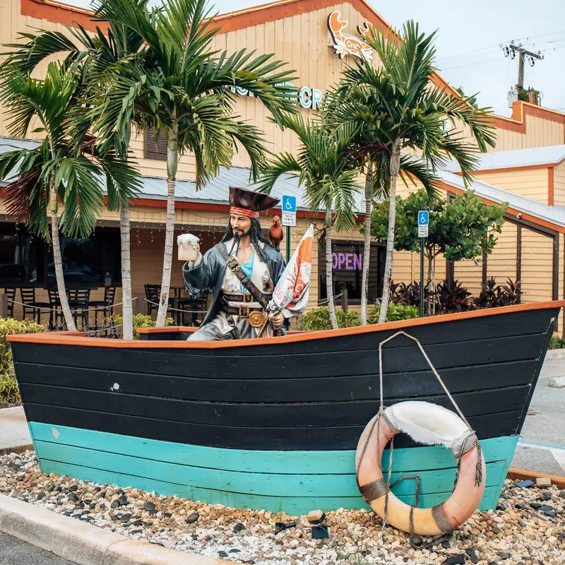 Outdoor decorative display featuring a life-sized pirate statue inside a painted wooden boat.