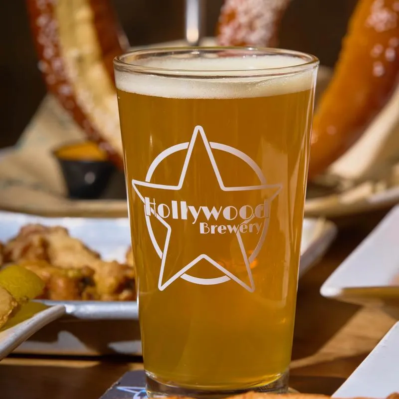 Pint of Hollywood Brewery beer surrounded by a large pretzel and pizza.