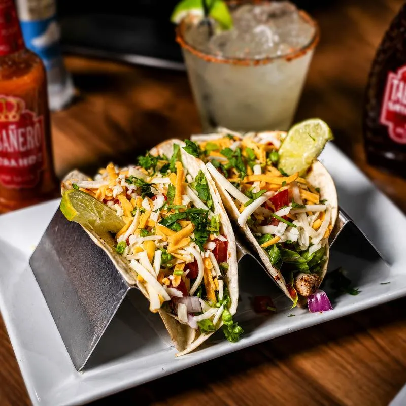 Chicken tacos served in a stainless steel holder on a white plate.