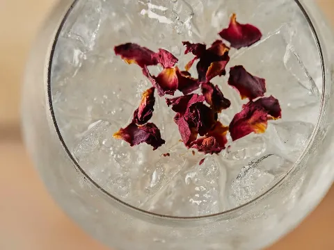 A glass with ice cubes and dried rose petals on top.