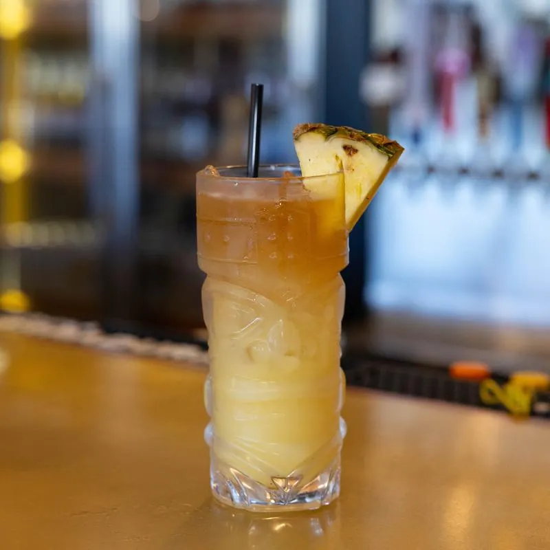 Cocktail in a tikki glass garnished with a slice of pineapple.