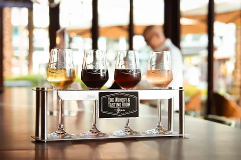 Four glasses of wine on a serving tray at a winery tasting room, with a blurred person in the background.