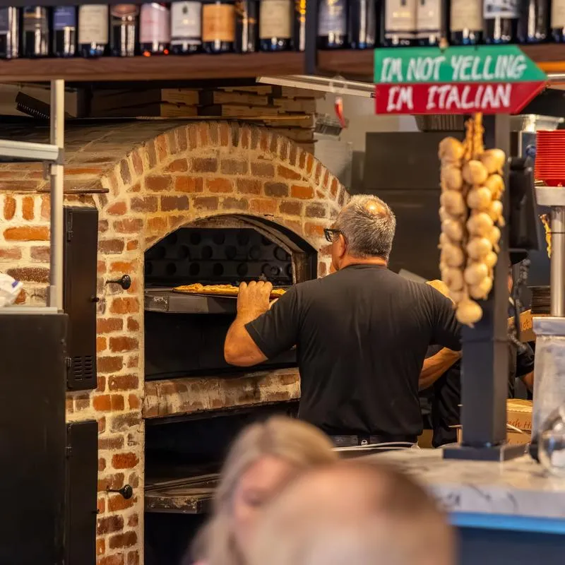 Chef sliding a pizza into a brick wood-fired oven.