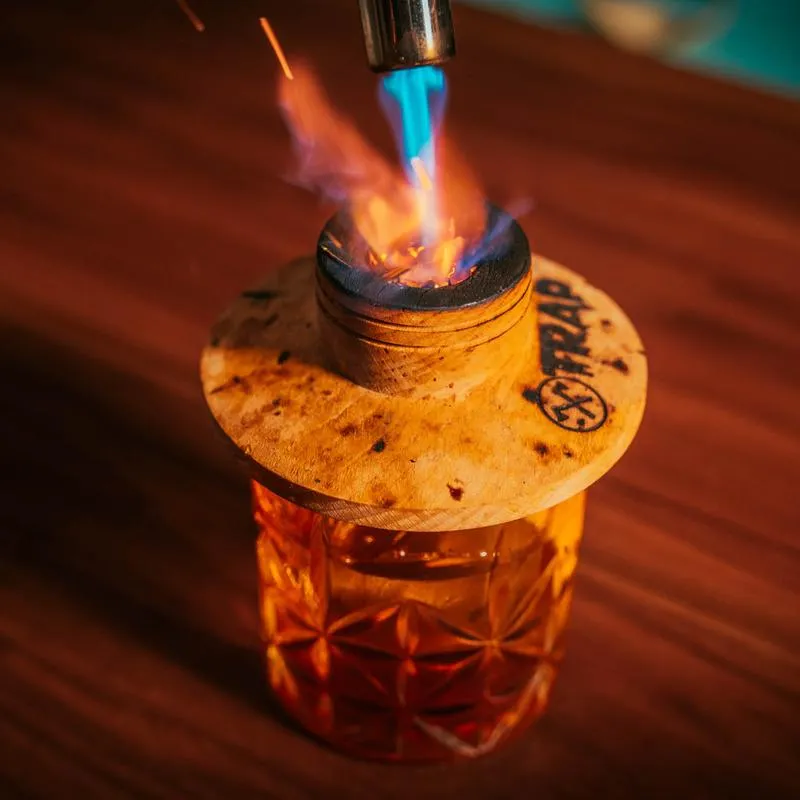 A smoky Old Fashioned cocktail with a smoker top being torched
