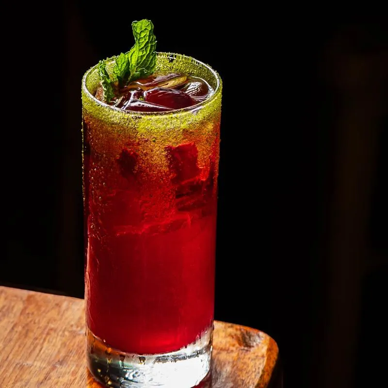 A red cocktail garnished with mint leaves.