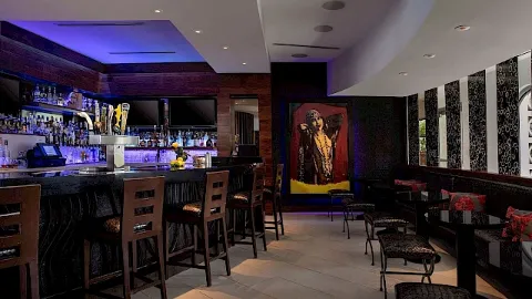 The image shows a stylish bar with high chairs, mood lighting, and wall art, creating a modern, cozy atmosphere.