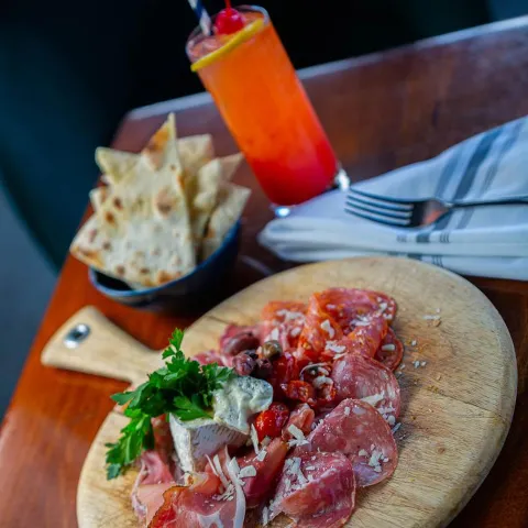 Board with cured meats, served with pita bowl and a cocktail drink