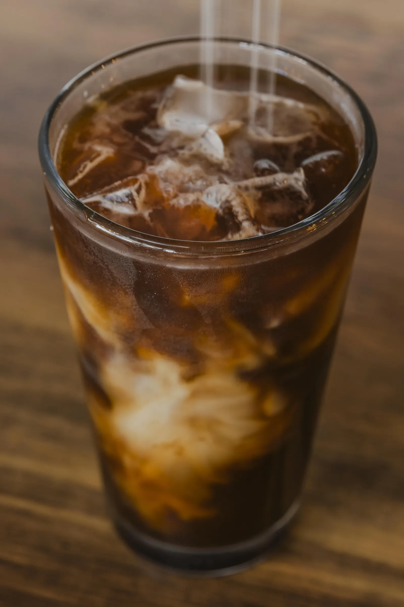A tall glass of iced coffee with ice cubes and swirling cream.