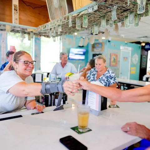 A friendly bartender hands out a drink to a customer over counter.