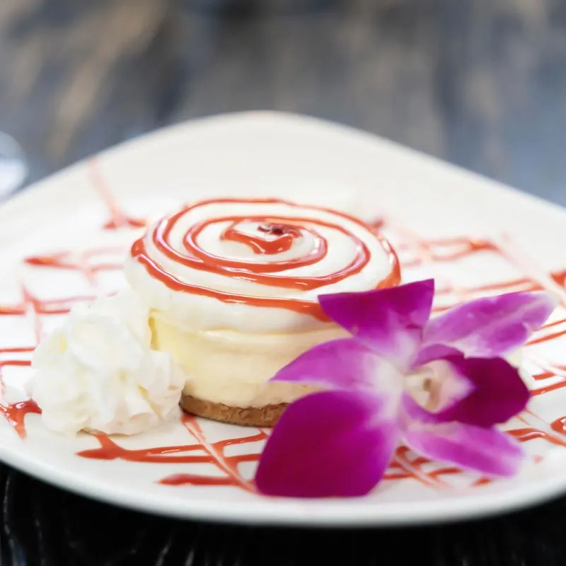 Raspberry cheesecake on a white plate with red fruit drizzle and whipped cream.