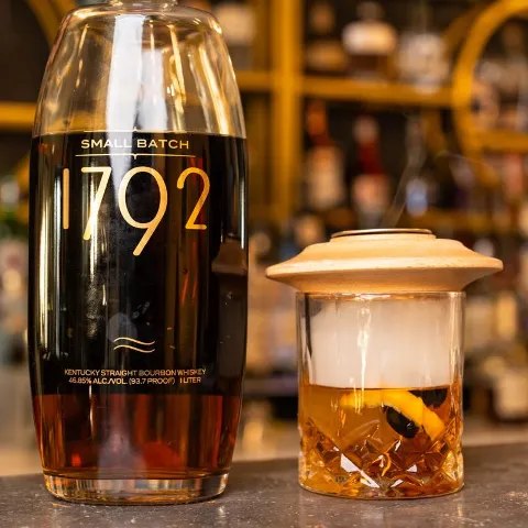 Cocktail being smoked on a counter, alongside a bottle of bourbon.