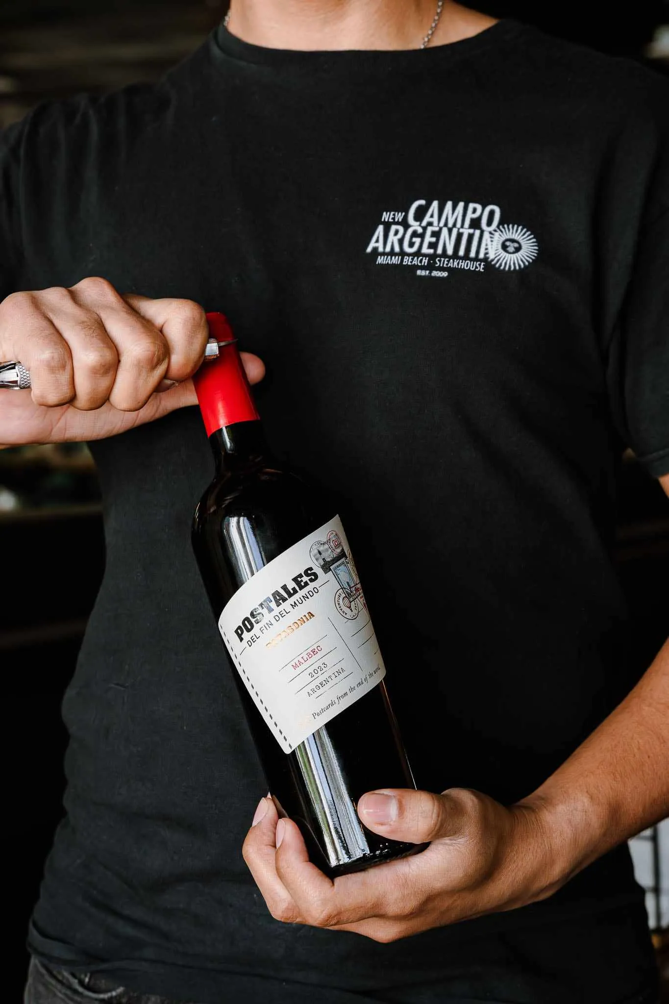 A server in a New Campo shirt holding a bottle of Catena Malbec