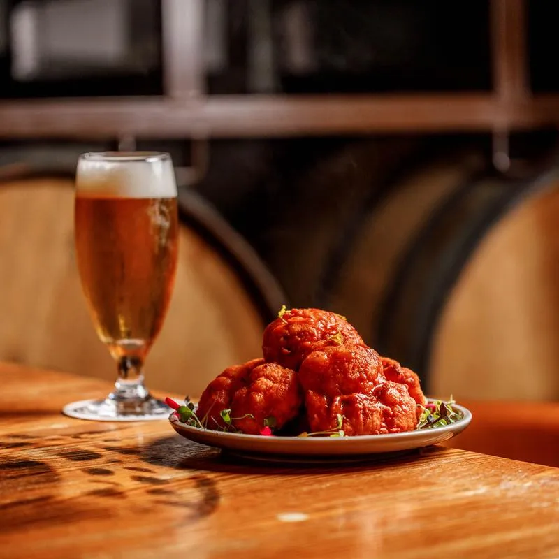 Buffalo cauliflower served with a glass of beer on a wooden table.