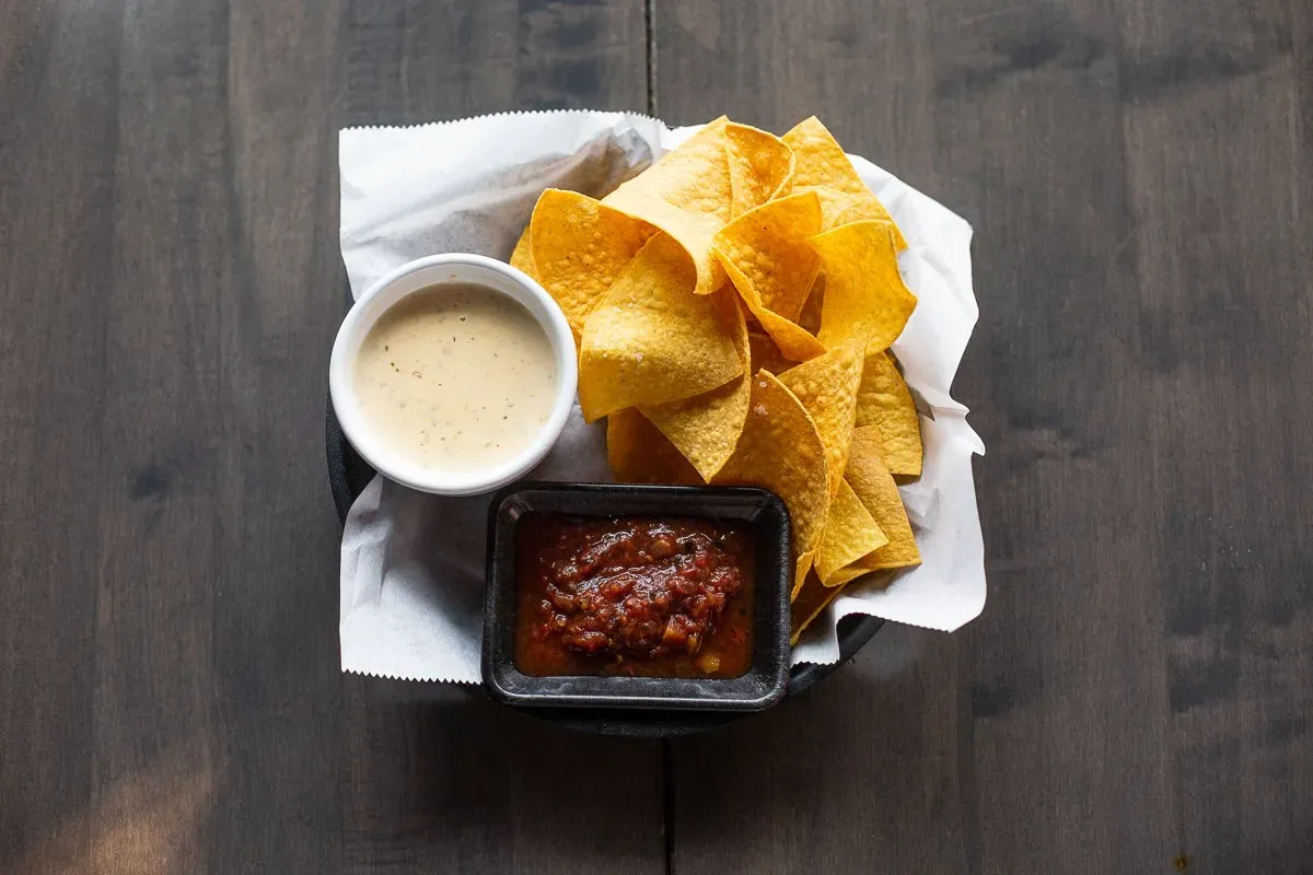 A bowl of tortilla chips and a bowl of salsa on a wooden table.