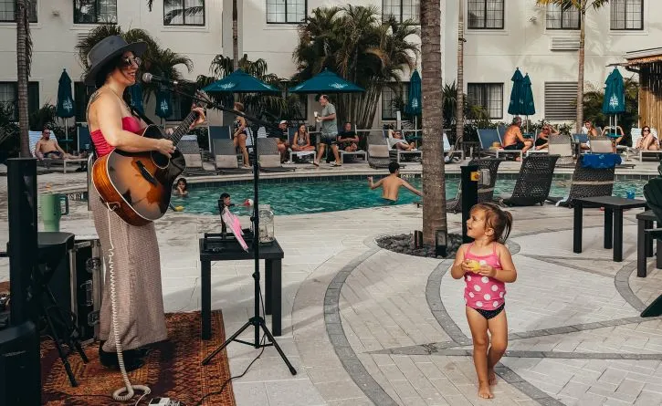A Person Playing A Guitar Next To A Girl Playing An Instrument