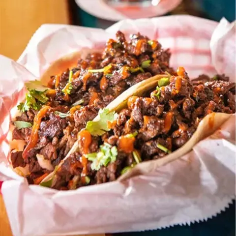 Two tacos filled with Korean BBQ beef, topped with cilantro and sauce, served in a paper-lined basket.
