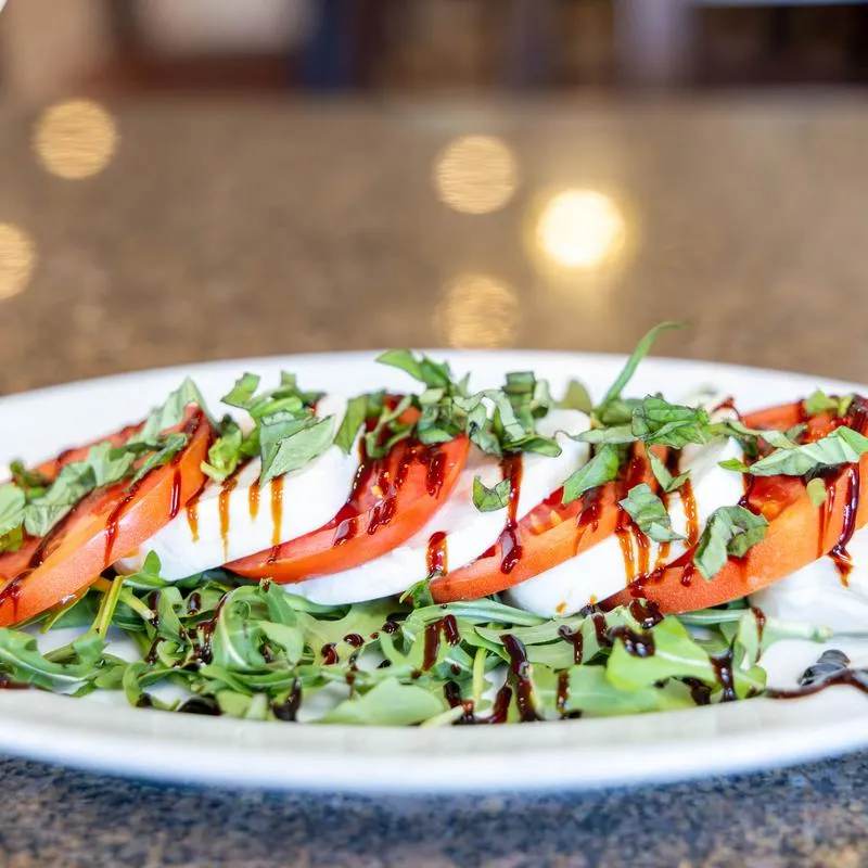 Caprese salad with tomato, mozzarella, and basil drizzled with a balsamic glaze.