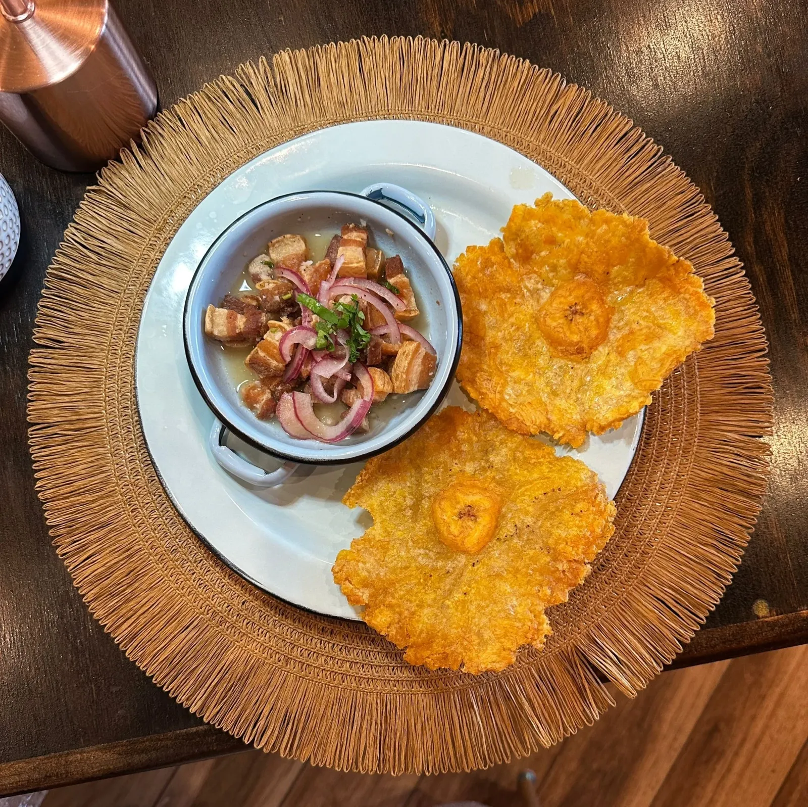 Fried fish fillets with a side of pork cracklings with onions and herbs on a white plate with a woven placemat.