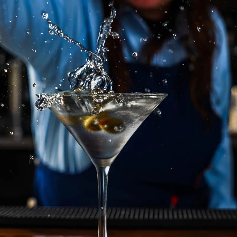 Green olives being dropped into the martini glass featuring a liquid splash.