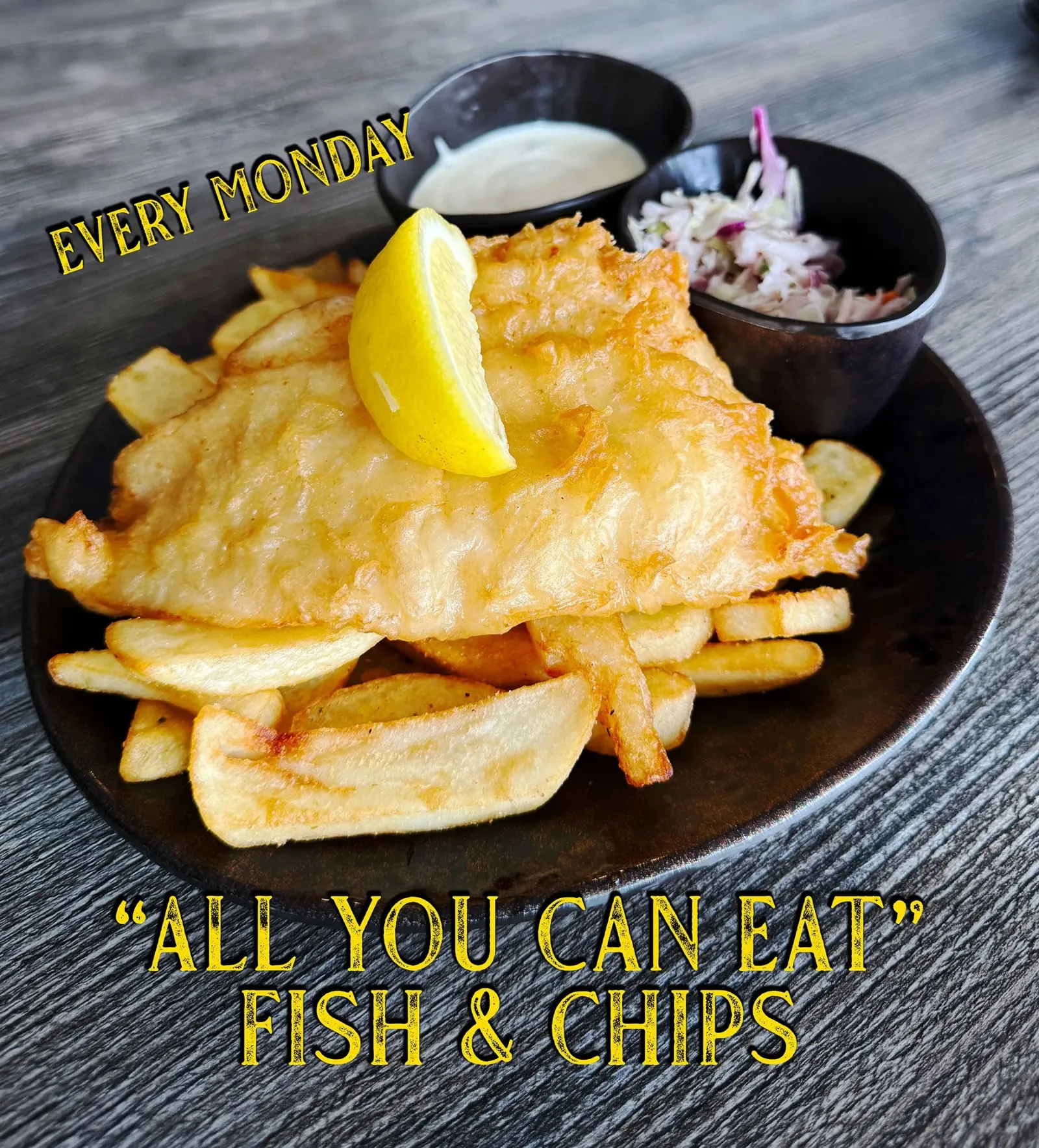 Plate of fish and chips with lemon wedge and two dipping sauces, one white and the other coleslaw, on a wooden table. Text overlay says 'Every Monday' and 'All You Can Eat' Fish & Chips."