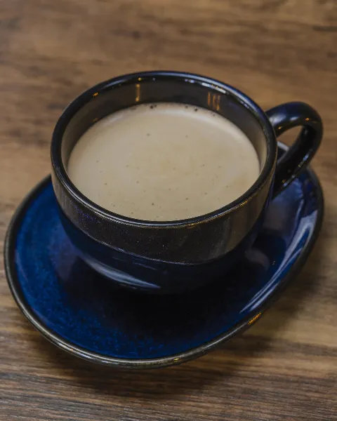 A cup of cafe con leche, hot espresso with milk in a blue cup on a saucer sitting on a wood table