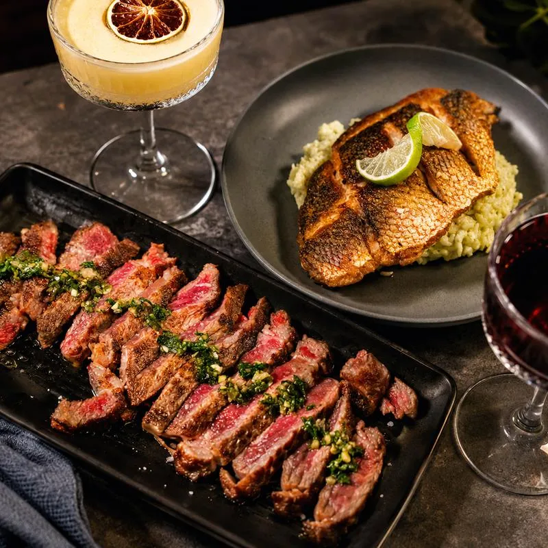 Seared ribeye slices, blackened fish, and a cocktail.