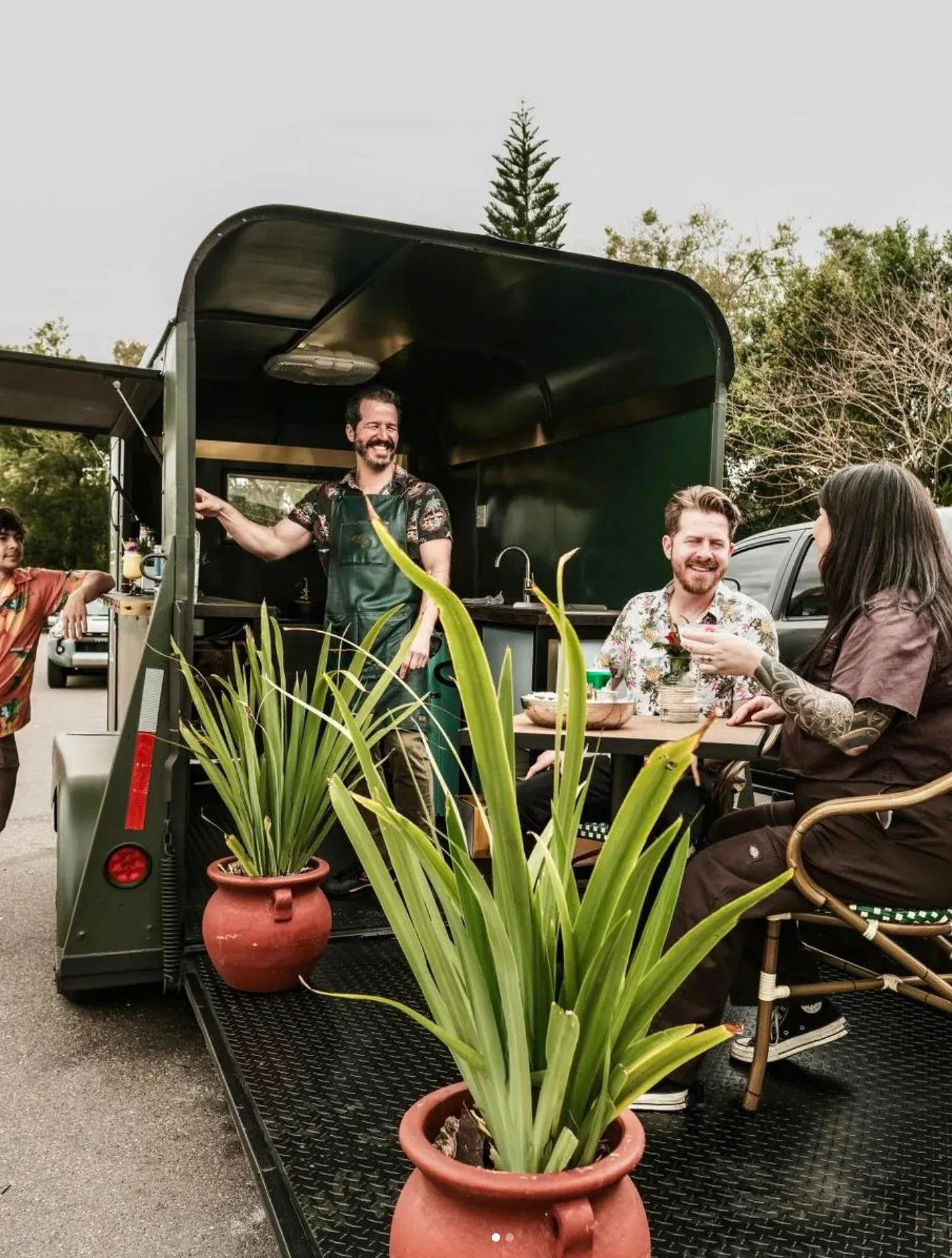 People enjoying a meal at a mobile food truck with potted plants in the foreground.