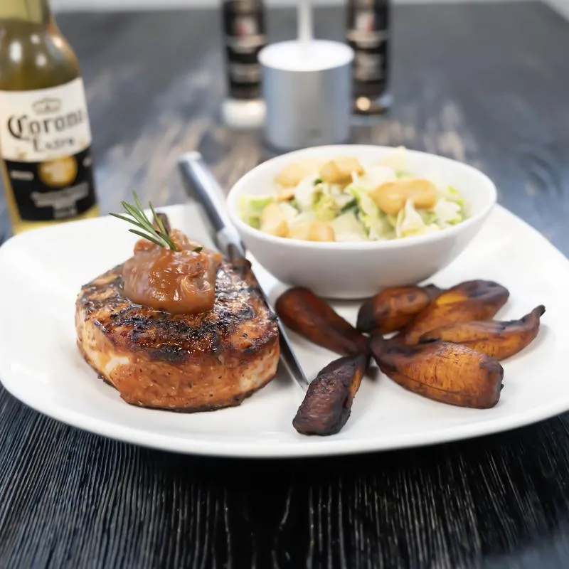 Grilled pork chop served with salad and roasted plantains.