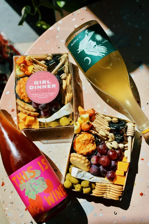 Two bottles of wine and two charcuterie boxes on a terrazzo surface.