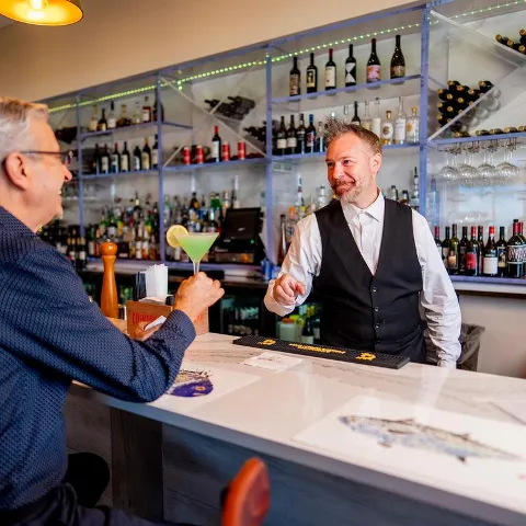 A bartender serving a green cocktail to a guest at a modern bar.