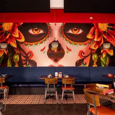 Interior, banquette with tables and chairs in front of a colorful wall mural