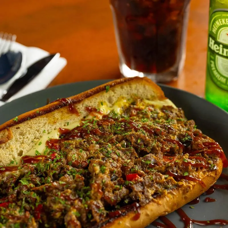 Philly cheesesteak sandwich with a soda and a beer.