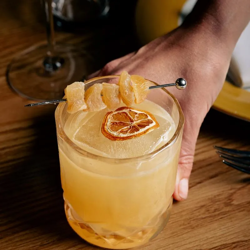 Penicillin cocktail garnished with candied ginger and dried lemon wheel.