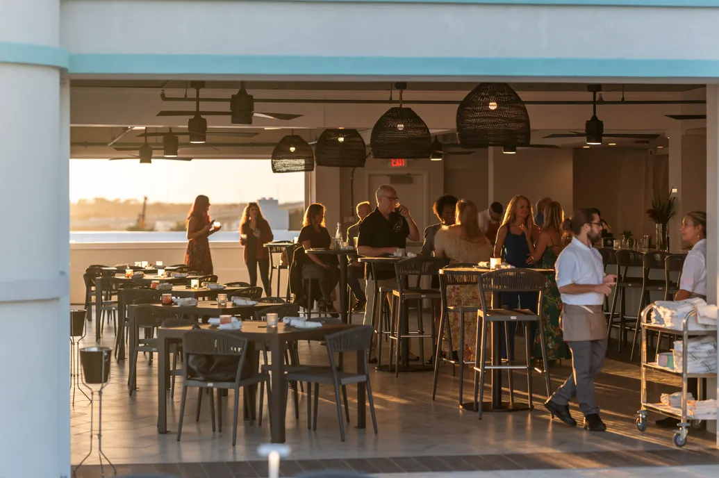 People socializing at an outdoor rooftop restaurant or bar during sunset.