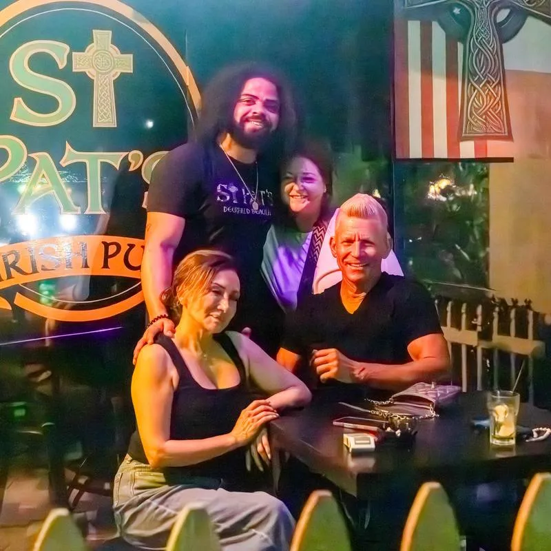 Group of people posing at the table with a pub's signage in the background.