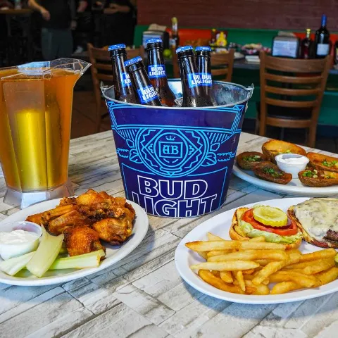 Beer bucket with bottles surrounded by plates of chicken wings, loaded potato skins, and fries.
