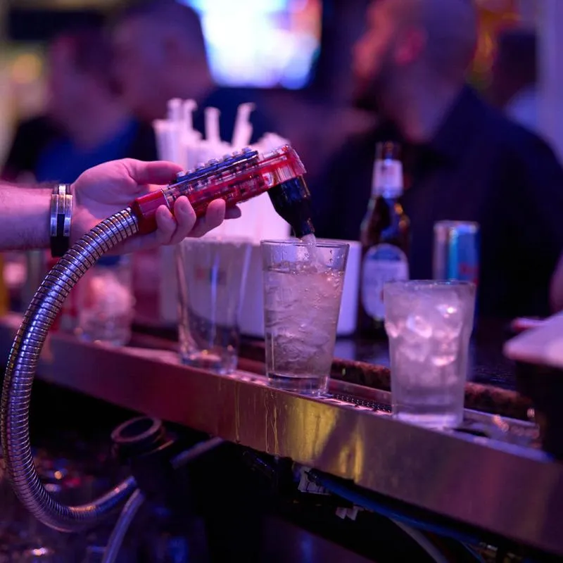Bartender pouring a drink from a soda gun into a glass at the bar.