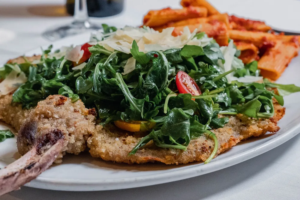 Breaded veal chop topped with arugula salad, with rigatoni