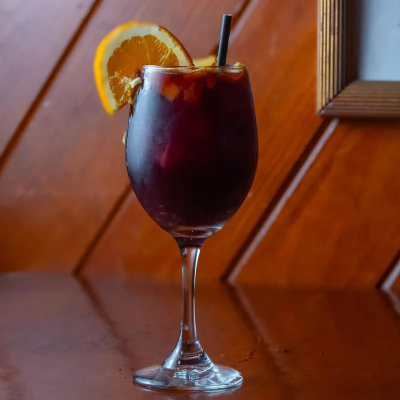 Glass of red sangria with orange slice garnish.