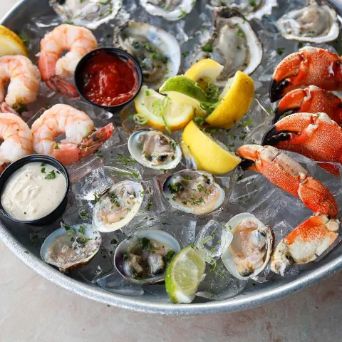 Seafood platter on ice with oysters, shrimp, lemon wedges, and cocktail sauce.