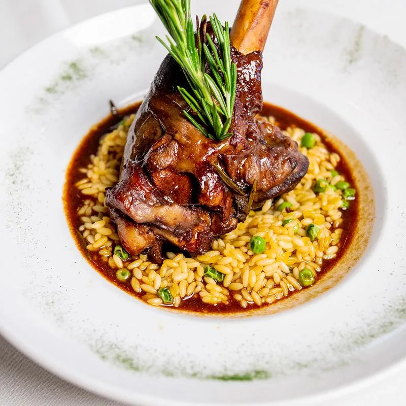 Braised lamb shank with orzo pasta, peas, brown sauce, and rosemary.