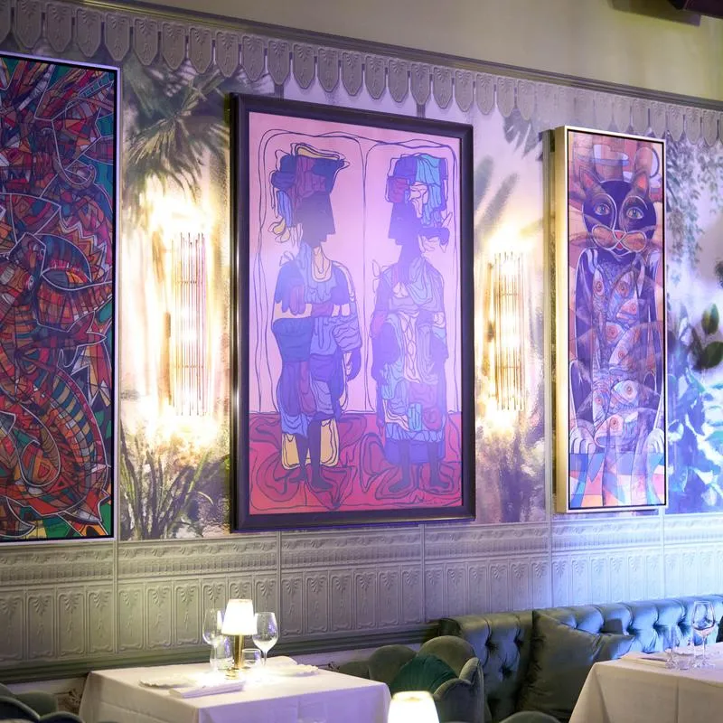 Colorful paintings above tables with white tablecloths.