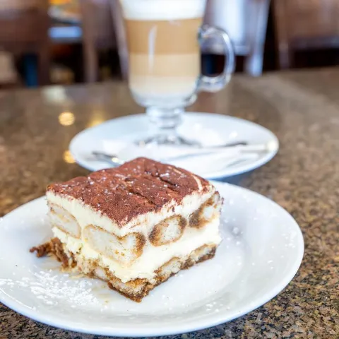 Tiramisu slice served with a layered coffee drink.