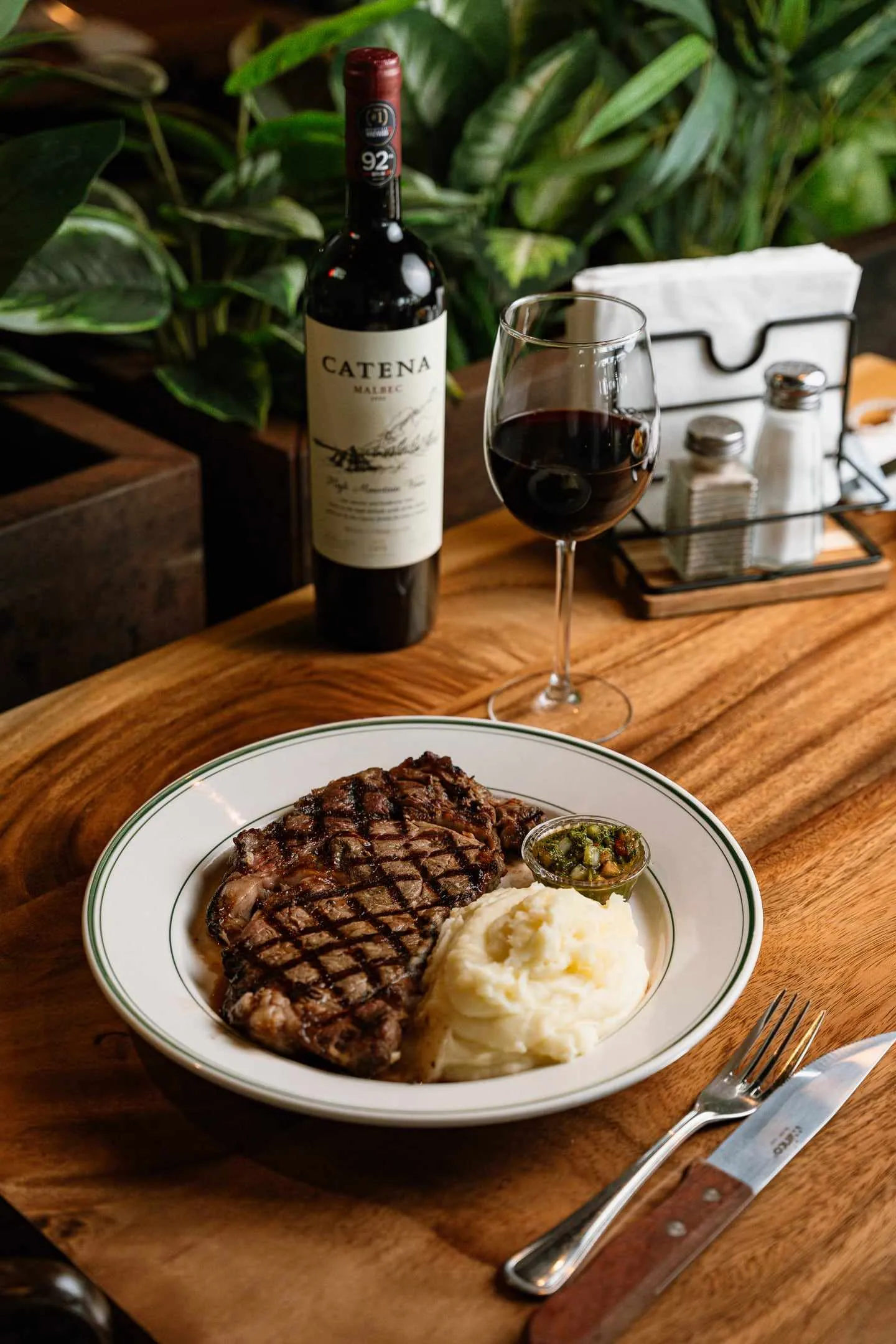 A grilled ribeye with mashed potatoes next to a bottle and a glass of Catena Malbec