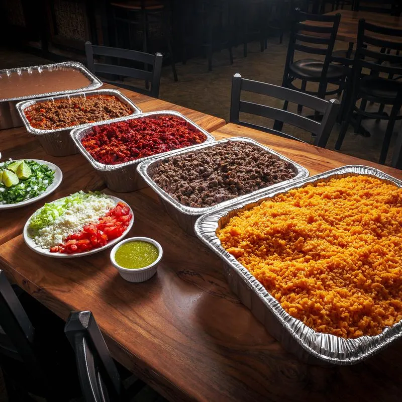 Mexican taco bar catering spread with various trays of food.
