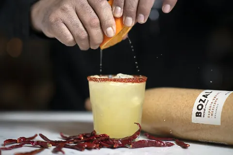A person is pouring orange juice into a glass of liquid.
