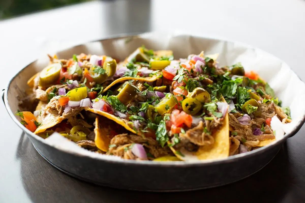 A bowl of nachos with meat and vegetables on a table.